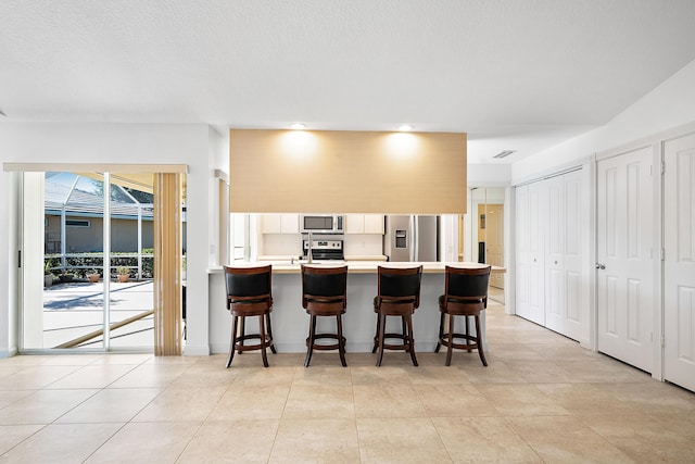 kitchen with a kitchen breakfast bar, kitchen peninsula, a textured ceiling, light tile patterned flooring, and appliances with stainless steel finishes