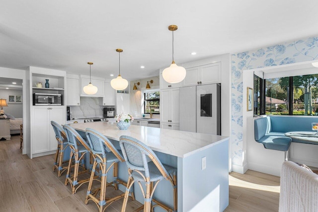 kitchen with hanging light fixtures, a kitchen island, light stone counters, fridge, and white cabinets