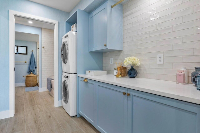 kitchen with light wood-type flooring, blue cabinetry, stacked washer / drying machine, and decorative backsplash