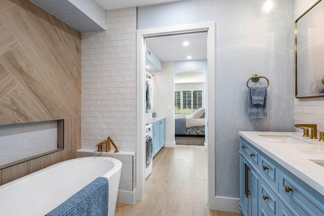 bathroom featuring a washtub, hardwood / wood-style flooring, vanity, and stacked washer / drying machine