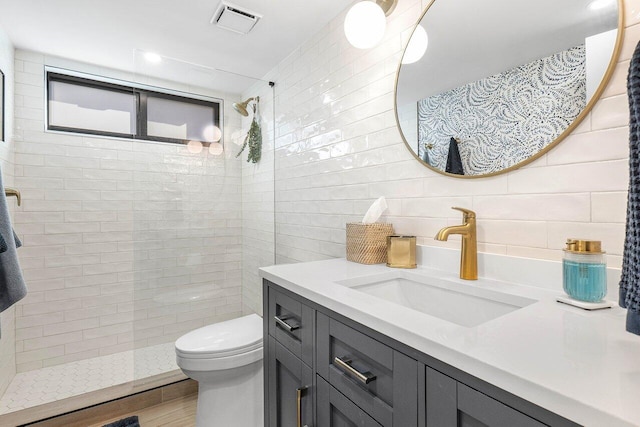 bathroom featuring toilet, tile walls, a tile shower, vanity, and decorative backsplash