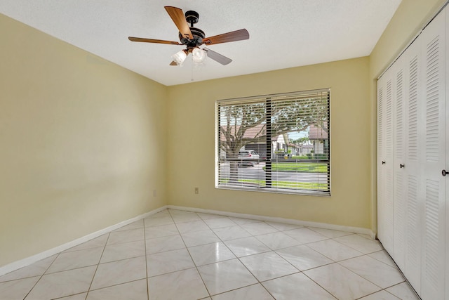 unfurnished bedroom with ceiling fan, a closet, light tile patterned flooring, and a textured ceiling