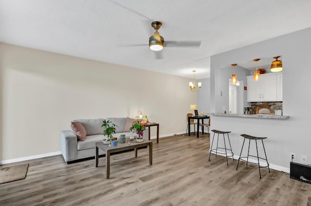 living room with ceiling fan with notable chandelier and light hardwood / wood-style floors