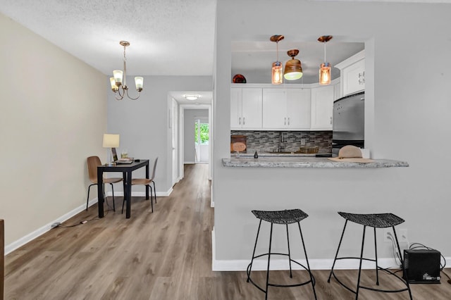 kitchen featuring decorative backsplash, stainless steel fridge, light stone countertops, decorative light fixtures, and white cabinetry