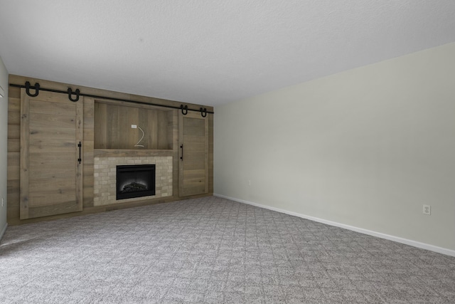 unfurnished living room with a barn door, a tiled fireplace, baseboards, and carpet flooring