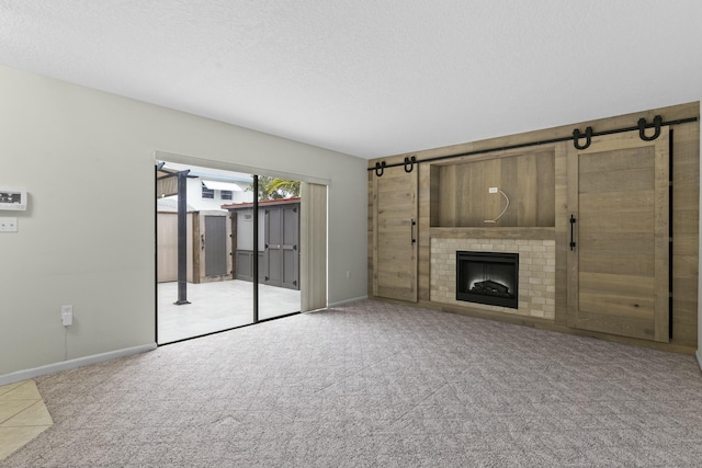 unfurnished living room featuring a barn door, baseboards, a textured ceiling, carpet flooring, and a fireplace