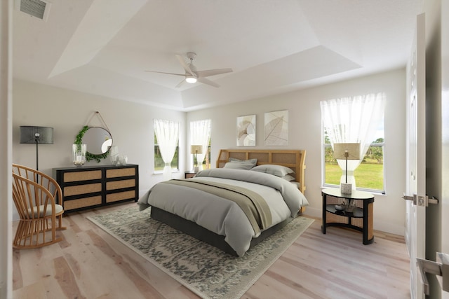 bedroom featuring a tray ceiling, multiple windows, ceiling fan, and light wood-type flooring