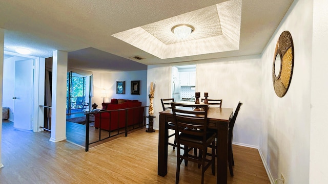 dining space with a raised ceiling, light hardwood / wood-style floors, and a textured ceiling