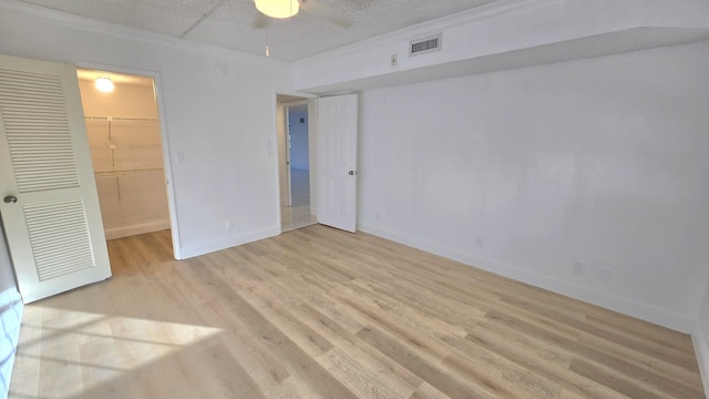 unfurnished bedroom featuring a spacious closet, a closet, ceiling fan, and light hardwood / wood-style flooring