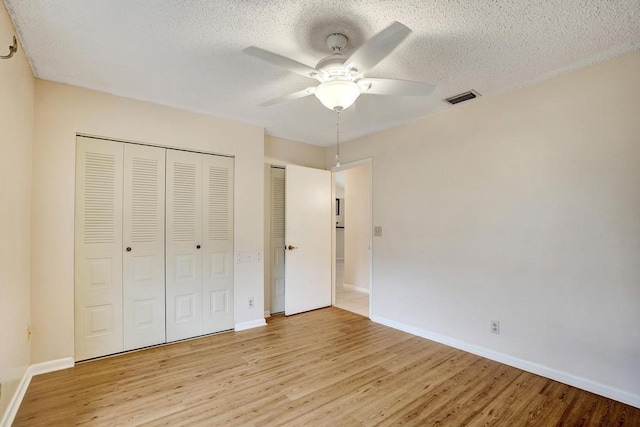 unfurnished bedroom with ceiling fan, light wood-type flooring, a textured ceiling, and two closets