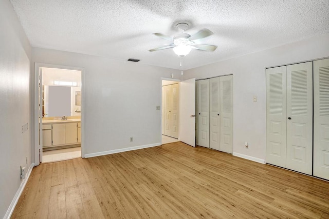 unfurnished bedroom with light wood-type flooring, ensuite bath, a textured ceiling, two closets, and ceiling fan