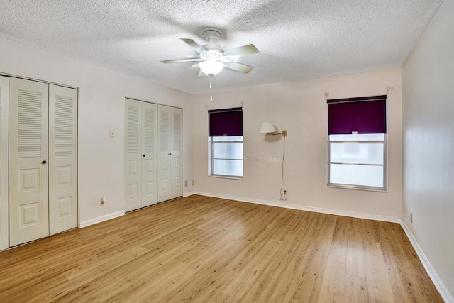 unfurnished bedroom with two closets, light hardwood / wood-style floors, multiple windows, and ceiling fan