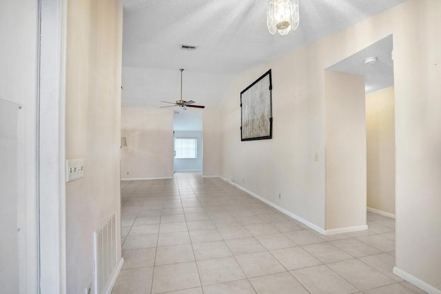 corridor featuring a textured ceiling, lofted ceiling, and light tile patterned flooring