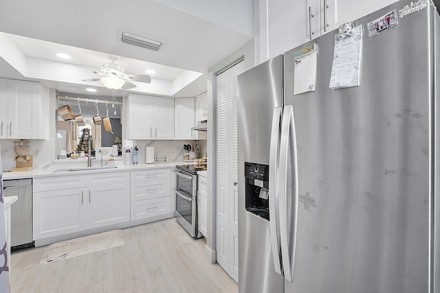 kitchen featuring stainless steel appliances, white cabinetry, a tray ceiling, and light hardwood / wood-style flooring