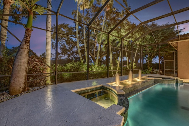 pool at dusk featuring a lanai and an in ground hot tub