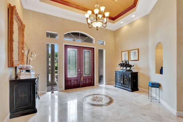 entrance foyer with a chandelier, a high ceiling, a raised ceiling, and ornamental molding