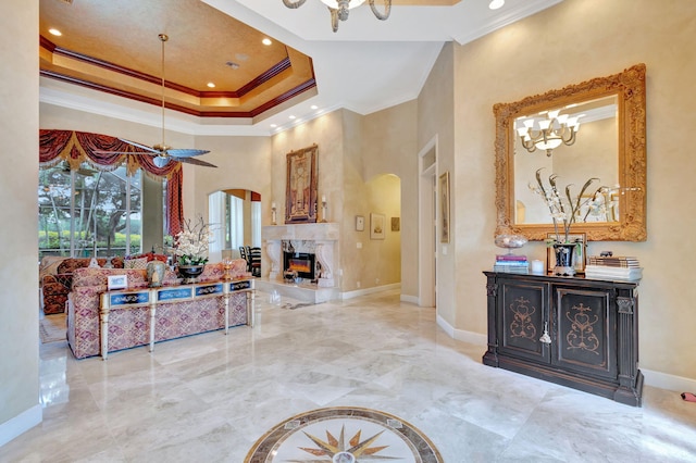 interior space with a high ceiling, a raised ceiling, a high end fireplace, ceiling fan with notable chandelier, and ornamental molding