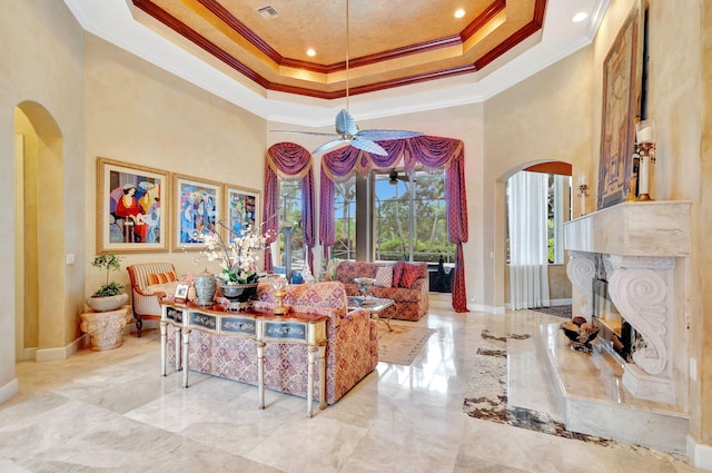 living room featuring a high end fireplace, a high ceiling, a tray ceiling, and crown molding