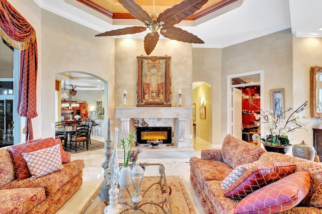 living room featuring ceiling fan, a high end fireplace, a towering ceiling, and ornamental molding