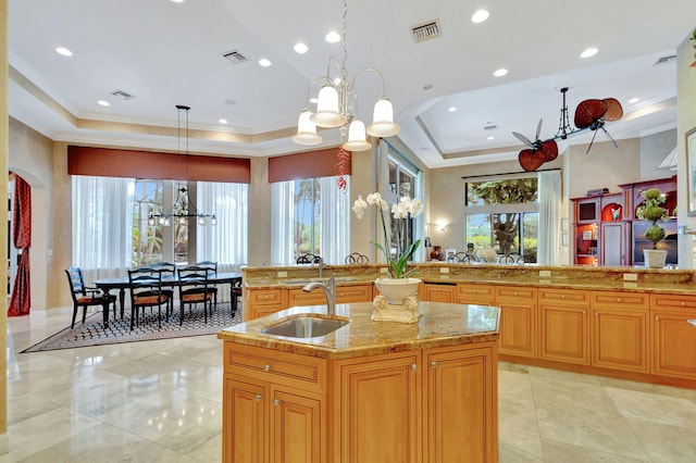 kitchen featuring pendant lighting, sink, an island with sink, a tray ceiling, and a notable chandelier