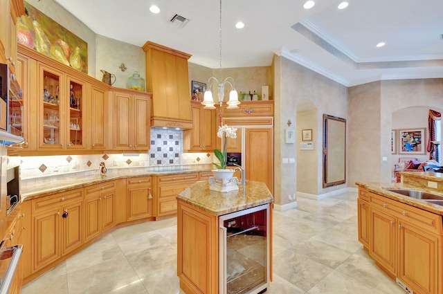 kitchen featuring black electric cooktop, beverage cooler, a center island with sink, a notable chandelier, and hanging light fixtures