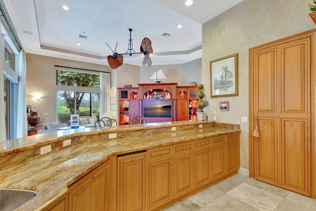 kitchen with light stone countertops, crown molding, light tile patterned floors, and a tray ceiling