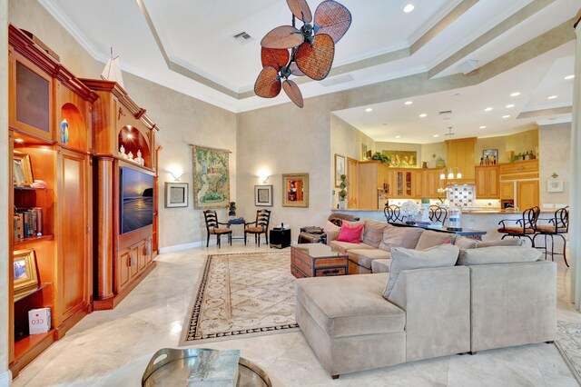 living room featuring a raised ceiling, ceiling fan, a towering ceiling, and ornamental molding