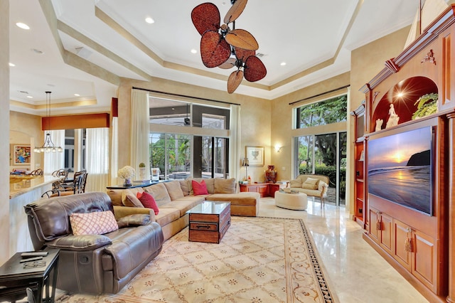 living room with a raised ceiling, ceiling fan, and ornamental molding