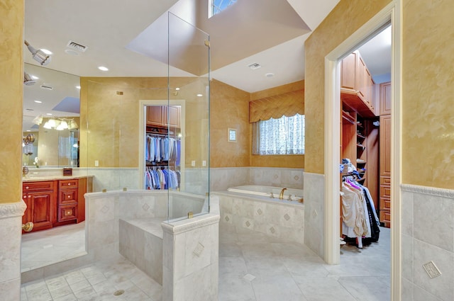 bathroom with tiled tub, tile patterned flooring, vanity, and tile walls