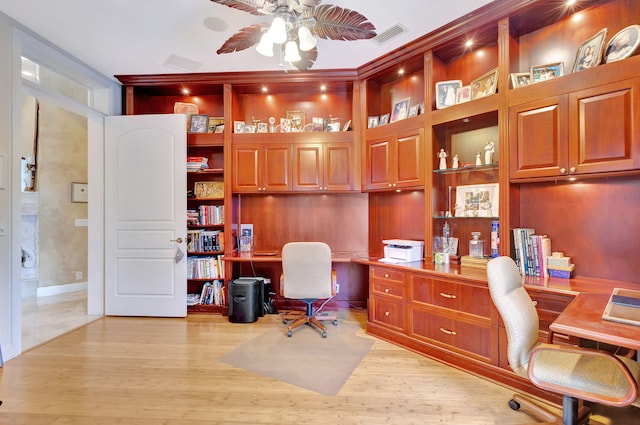 home office featuring built in shelves, built in desk, light hardwood / wood-style floors, and ceiling fan