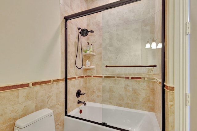 bathroom with shower / bath combination with glass door, toilet, and tile walls