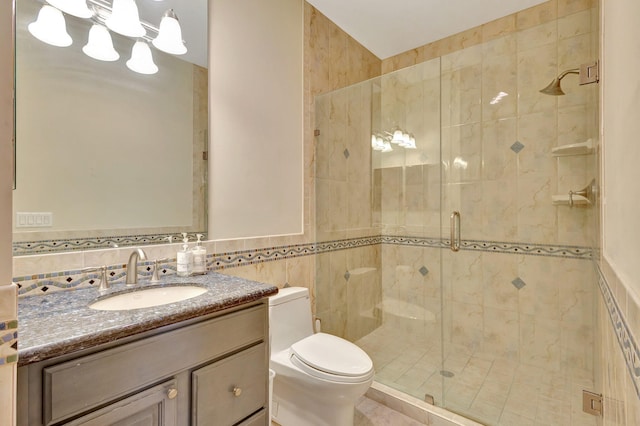 bathroom featuring vanity, toilet, a shower with door, and tile walls