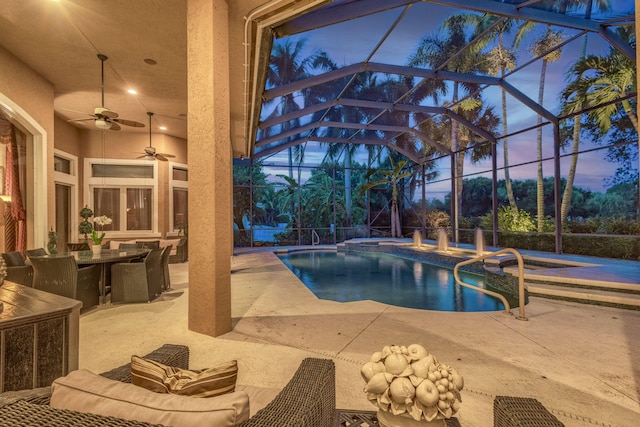 pool at dusk featuring ceiling fan, a patio area, a lanai, and an in ground hot tub