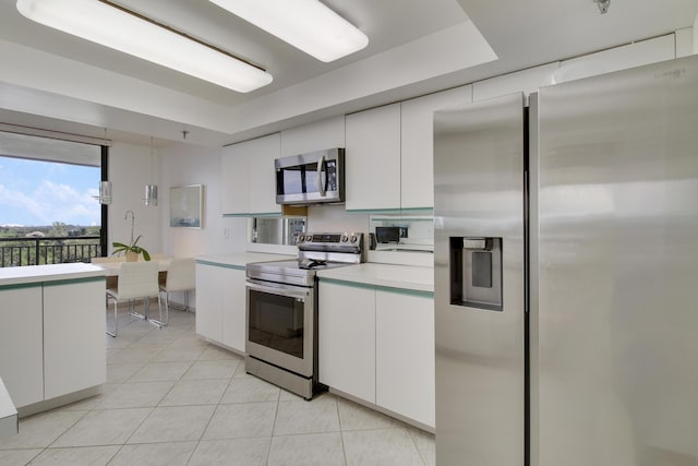 kitchen with white cabinets, light tile patterned floors, stainless steel appliances, and a tray ceiling