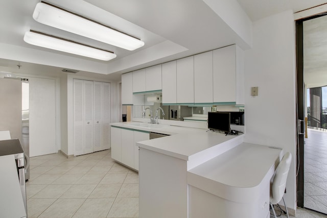 kitchen with white cabinetry, sink, kitchen peninsula, fridge, and light tile patterned floors