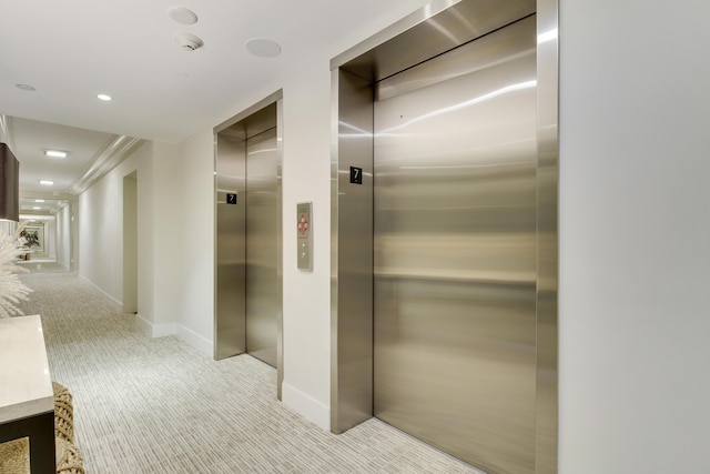 hallway with elevator and light carpet