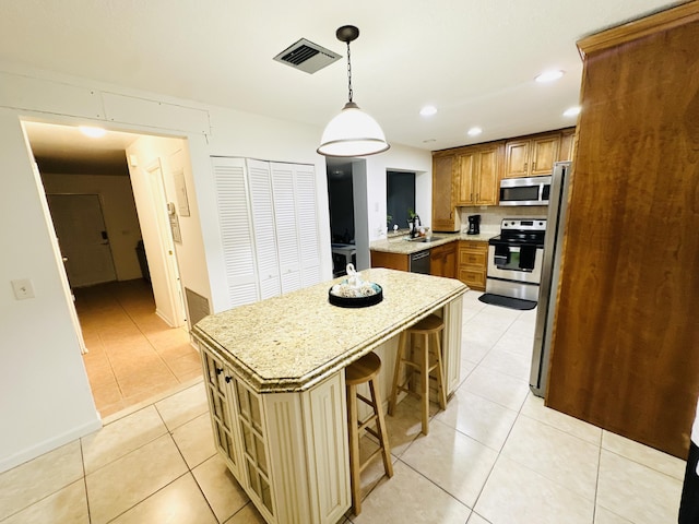 kitchen with appliances with stainless steel finishes, a kitchen breakfast bar, light tile patterned floors, decorative light fixtures, and a center island