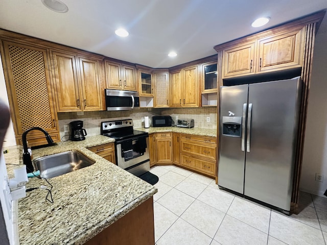 kitchen featuring light stone countertops, appliances with stainless steel finishes, backsplash, sink, and light tile patterned floors