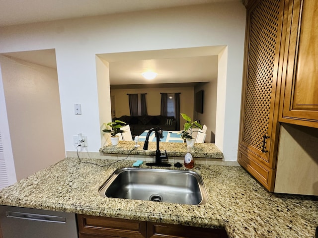 kitchen with stainless steel dishwasher, kitchen peninsula, light stone countertops, and sink