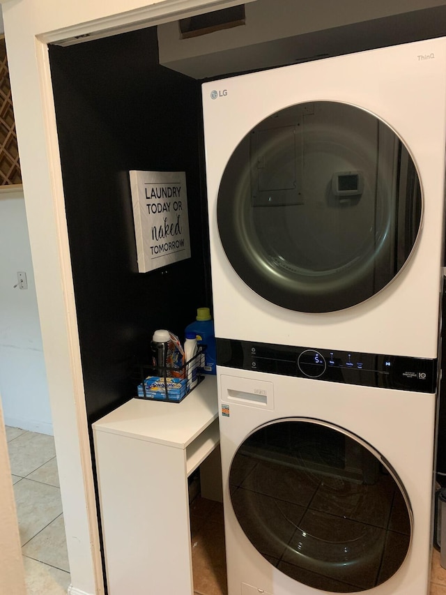 laundry area with light tile patterned floors and stacked washing maching and dryer