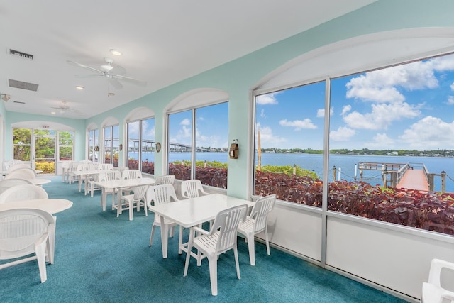 sunroom with ceiling fan and a water view