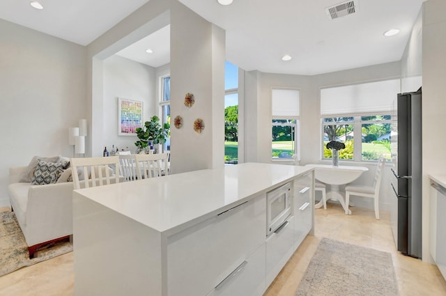 kitchen with stainless steel fridge, white microwave, light tile patterned floors, a center island, and white cabinetry