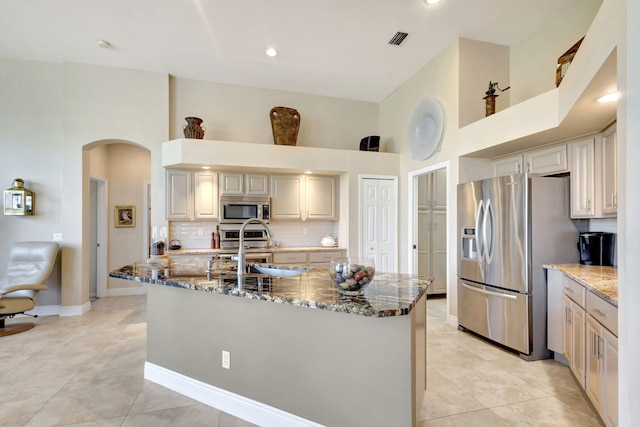 kitchen featuring a towering ceiling, dark stone countertops, decorative backsplash, a large island, and stainless steel appliances