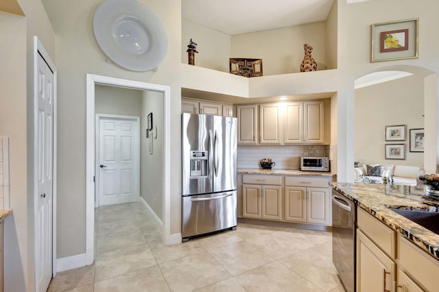 kitchen featuring decorative backsplash, stainless steel appliances, light brown cabinets, and a high ceiling