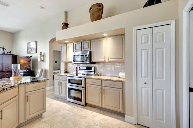 kitchen featuring tasteful backsplash, appliances with stainless steel finishes, light stone countertops, and cream cabinetry