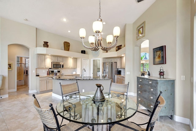 tiled dining space featuring an inviting chandelier, a towering ceiling, and sink