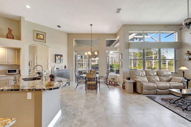 kitchen with pendant lighting, sink, dark stone countertops, a towering ceiling, and ceiling fan with notable chandelier