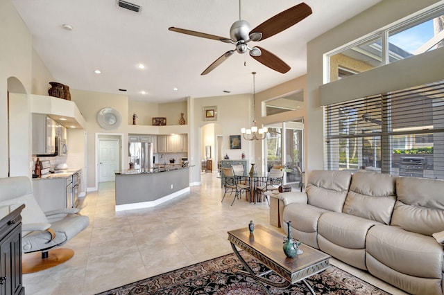 tiled living room with a towering ceiling and ceiling fan with notable chandelier