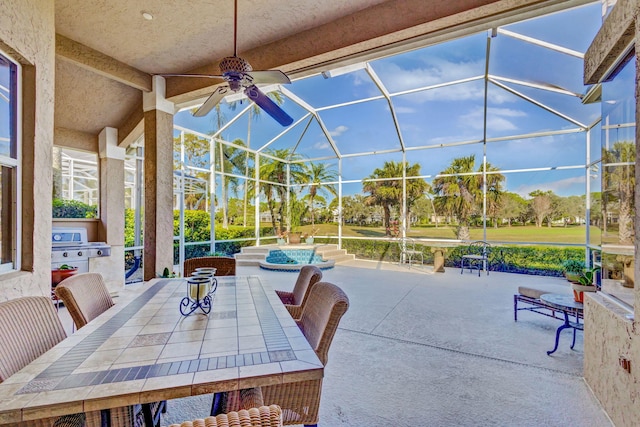 view of patio with ceiling fan, glass enclosure, area for grilling, a jacuzzi, and an outdoor kitchen