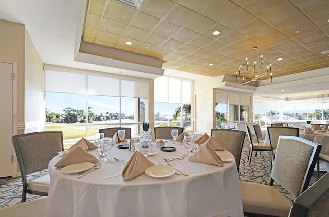 dining area with expansive windows, a raised ceiling, a drop ceiling, and a notable chandelier